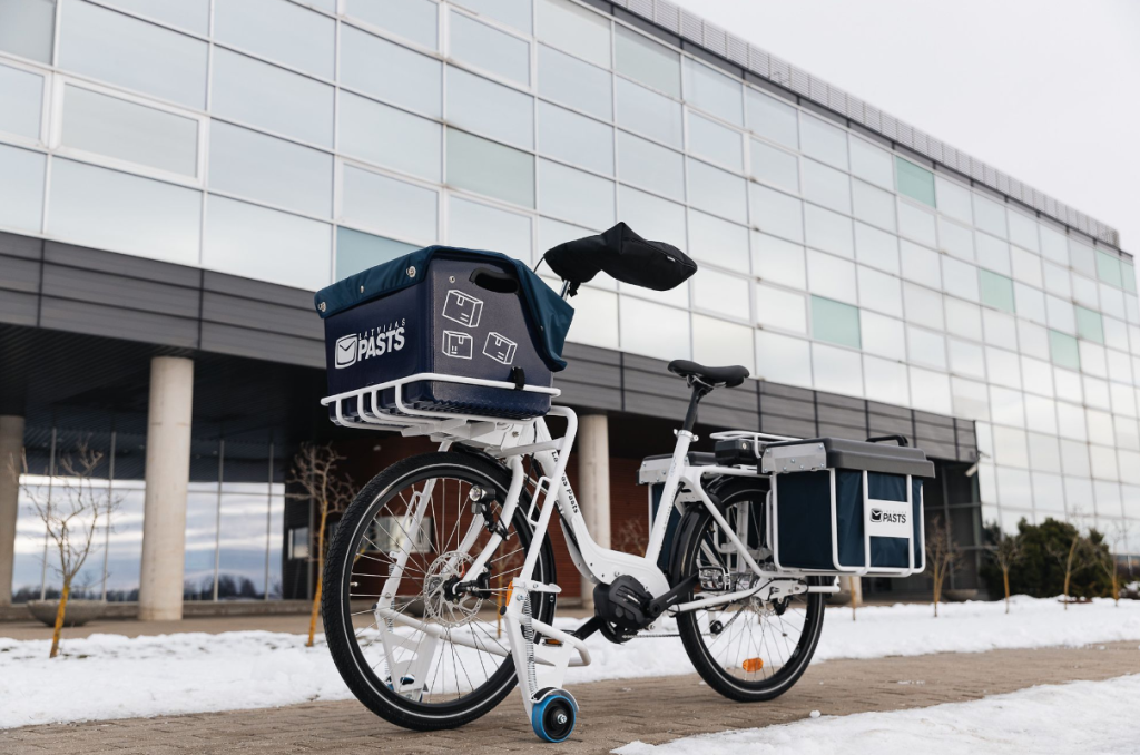 A white Latvijas Pasts e-bike outside on the sidewalk.