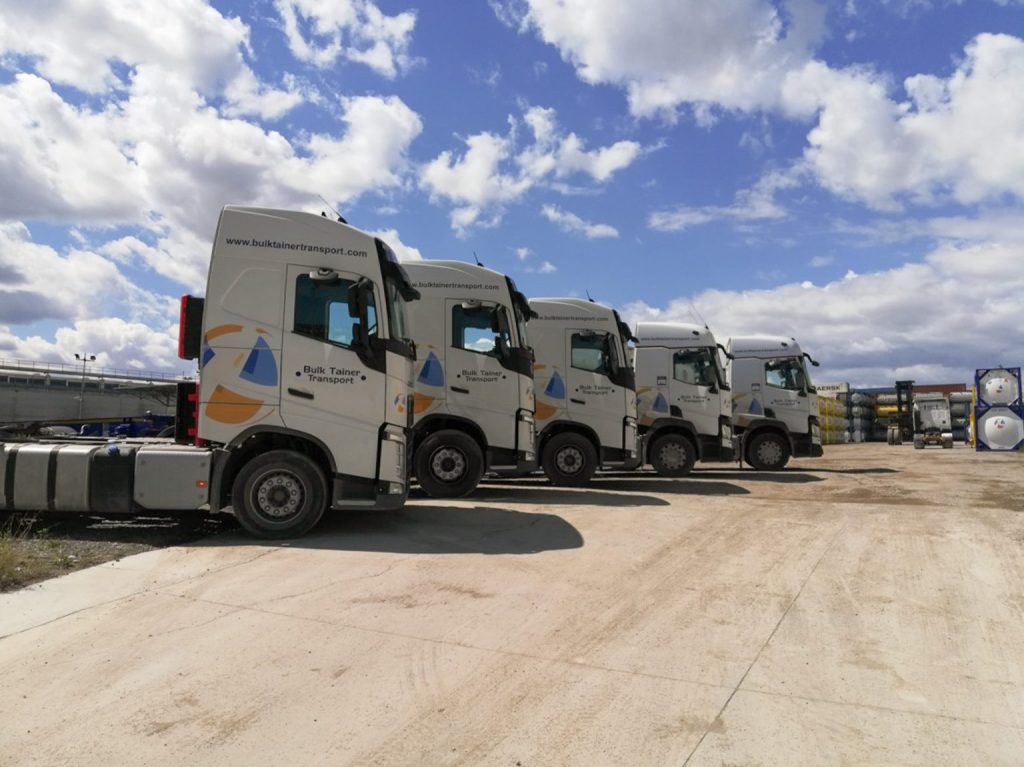 Several white Bulk Tainer trucks without trailers parked outside.
