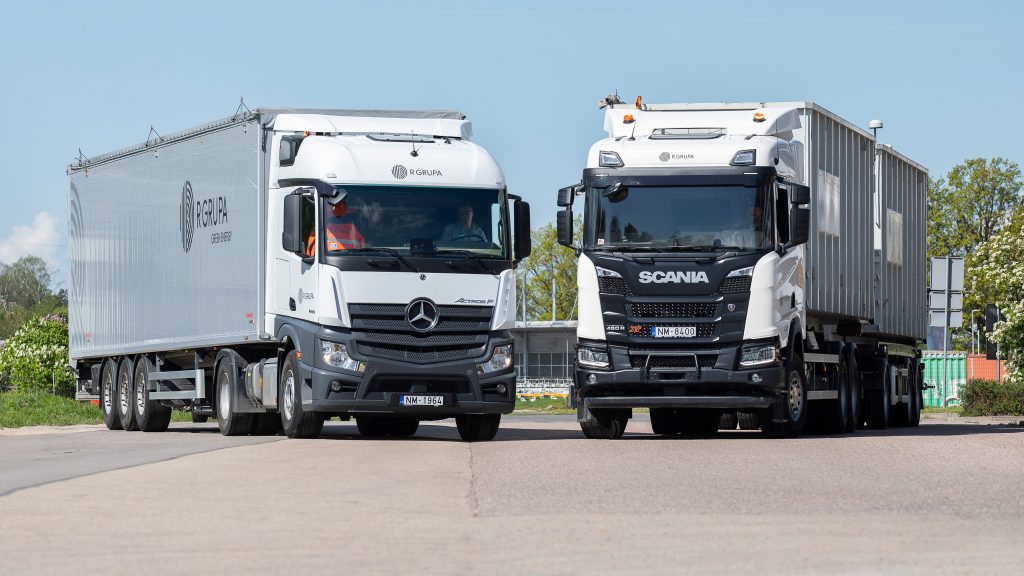 Two white trucks with R GRUPA logos stand on the road at an angle to each other.
