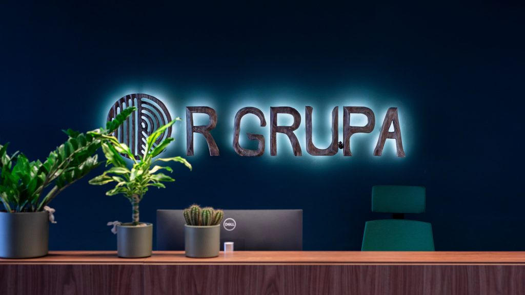 The R GRUPA’s logo on a blue wall above a table in the company office.
