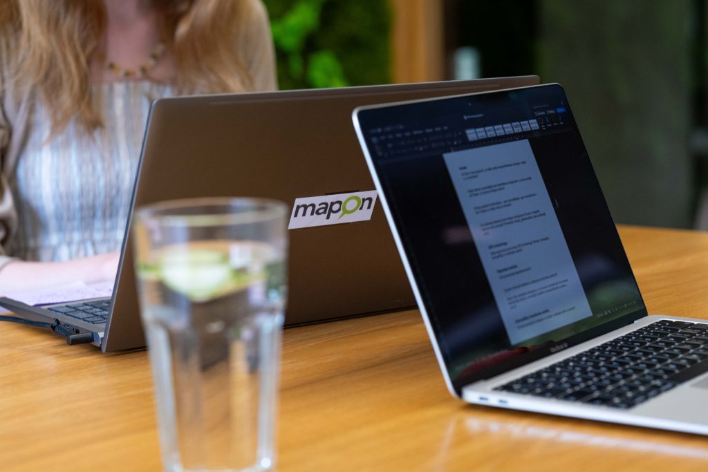 A work desk with two open laptops. A glass of water is in the foreground, while a person can be seen in the background, preparing for an interview.