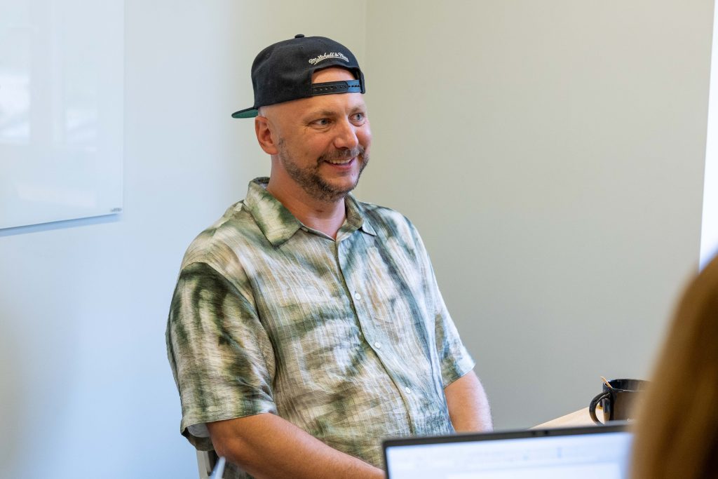 A truck driver shares his experience with fleet management solutions, seating at an office desk against a plain backdrop.