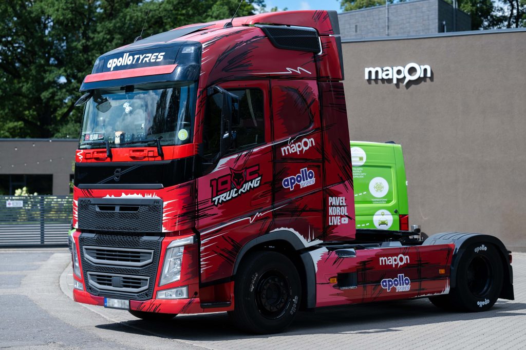 A red truck with the 19.05 logo parked outside Mapon's office, with the Mapon's logo visible on the building's exterior.