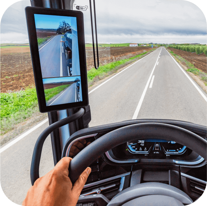 Skats uz kravas automašīnas kabīni, kur redzams monitors, kas pieslēgts pie kameru sistēmas, nodrošinot vadītājam sānu skatu uz ceļu.