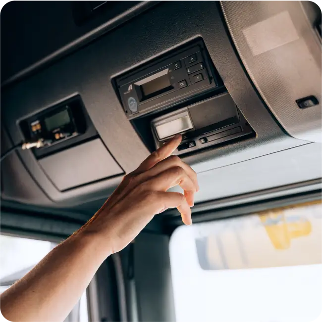 A driver in the cab holding out his hand to a digital tachograph performing tachograph remote download.