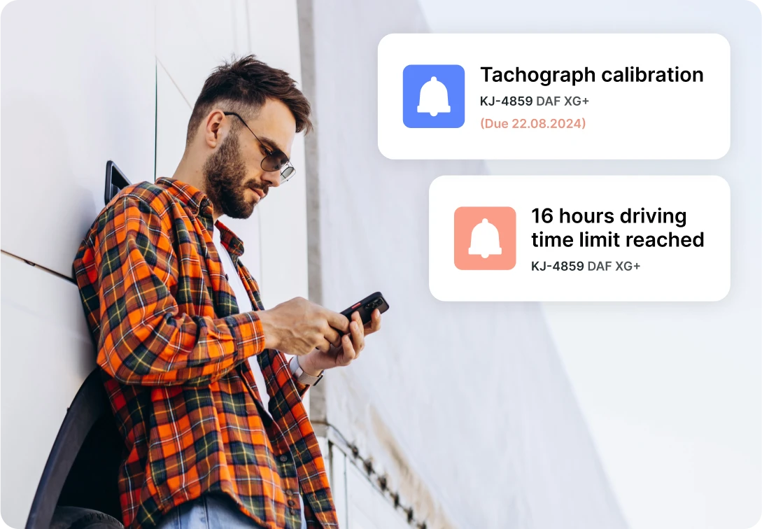 A person standing next to a white wall checking his phone for tachograph alerts on calibration dates and driving time limits.