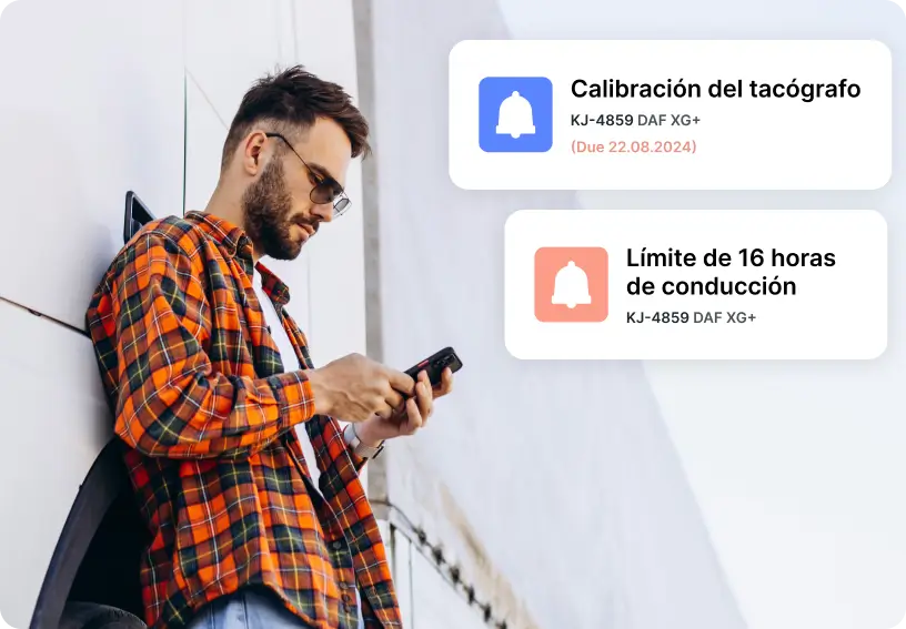 Una persona de pie junto a una pared blanca comprobando en su teléfono las alertas del tacógrafo sobre fechas de calibración y límites de tiempo de conducción.