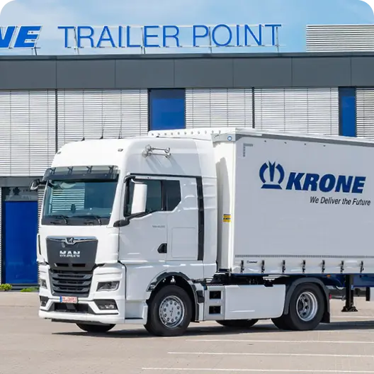 A white truck with a white KRONE trailer parked in front of KRONE facilities.