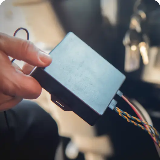 A person holding the Mapon Expert GPS fleet tracker, which is attached to a vehicle. 